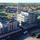 Aerial view of a newly completed mid rise apartment development with brick facades, balconies and ground floor commercial units, set within an active residential neighbourhood with surrounding housing, roads and ongoing construction works visible.